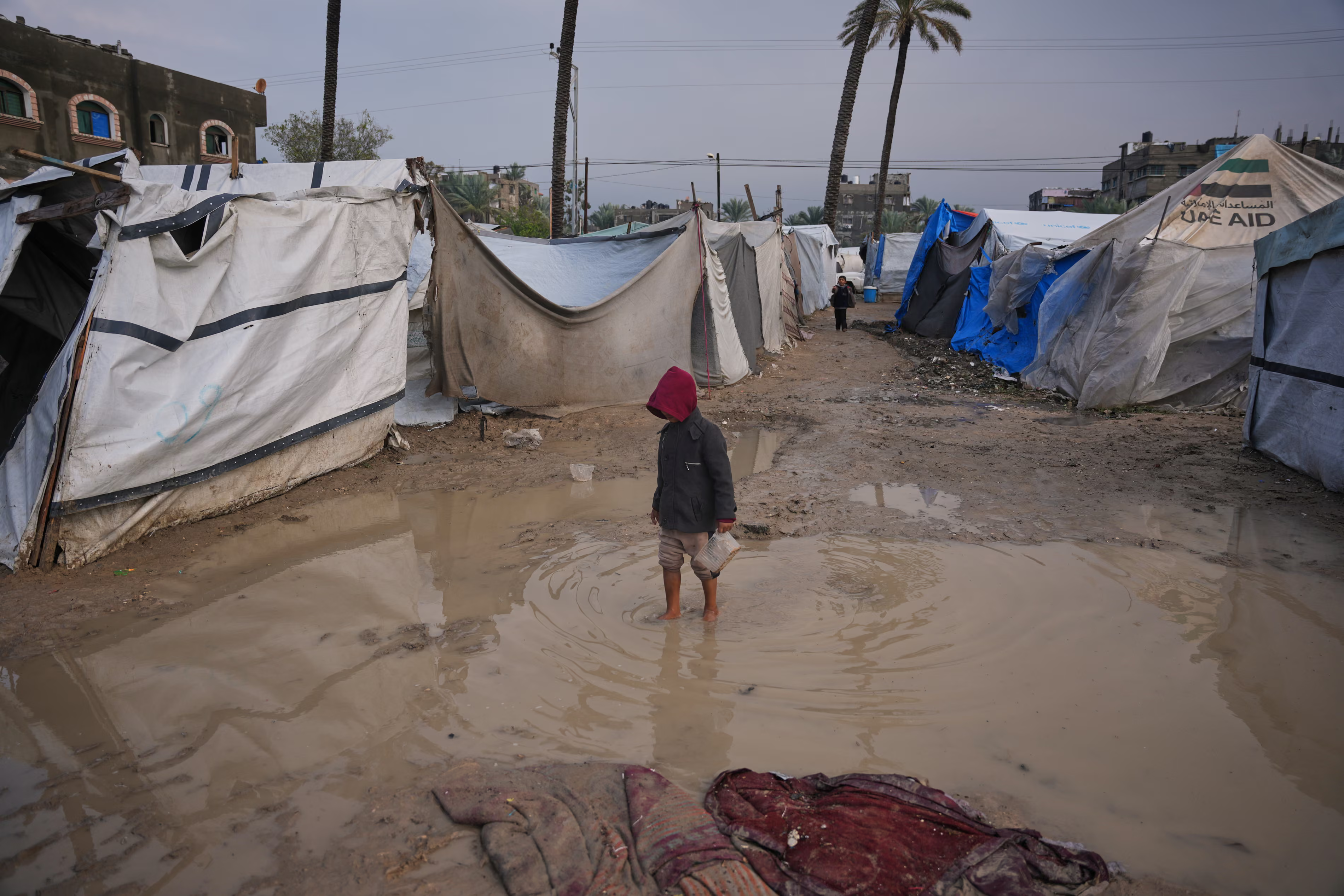 A child stands in a puddle between flooded tents in Gaza
