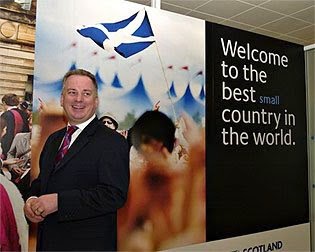 Jack McConnell, pictured in front of a poster reading 'Welcome to the best small country in the world'