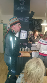 Pete White, in impossibly bling retro-reflective jacket, buys coffee in the unknown coffee shop. 
