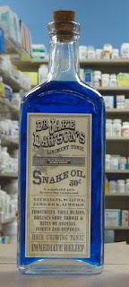 A blue glass bottle, bearing a faded, Victorian-looking label saying 'Snake Oil'