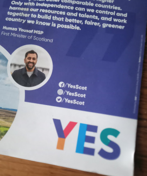 Corner of a leaflet, showing Humza Yousaf's face, a multicoloured 'Yes' logo, and 'Yes Scot' social media links.