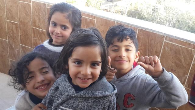 A group of three small girls and one small boy, grinning up at the camera