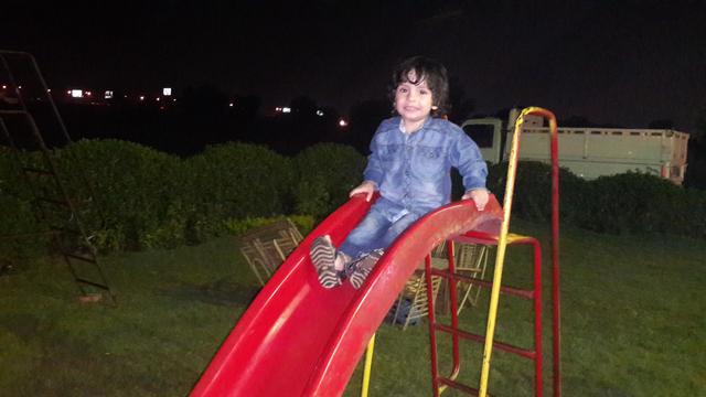 A young boy (Ady?) on a red plastic slide, at night.