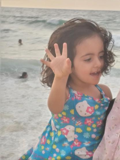 Kinda, as a young child in a blue bathing costume, on the shore.
