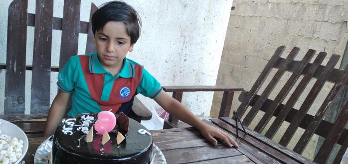 A small boy (Ady?) looking at a birthday cake on a plate on the garden table.
