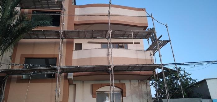 A small two storey house with walls rendered in warm earth colours, almost complete, with scaffolding still around it