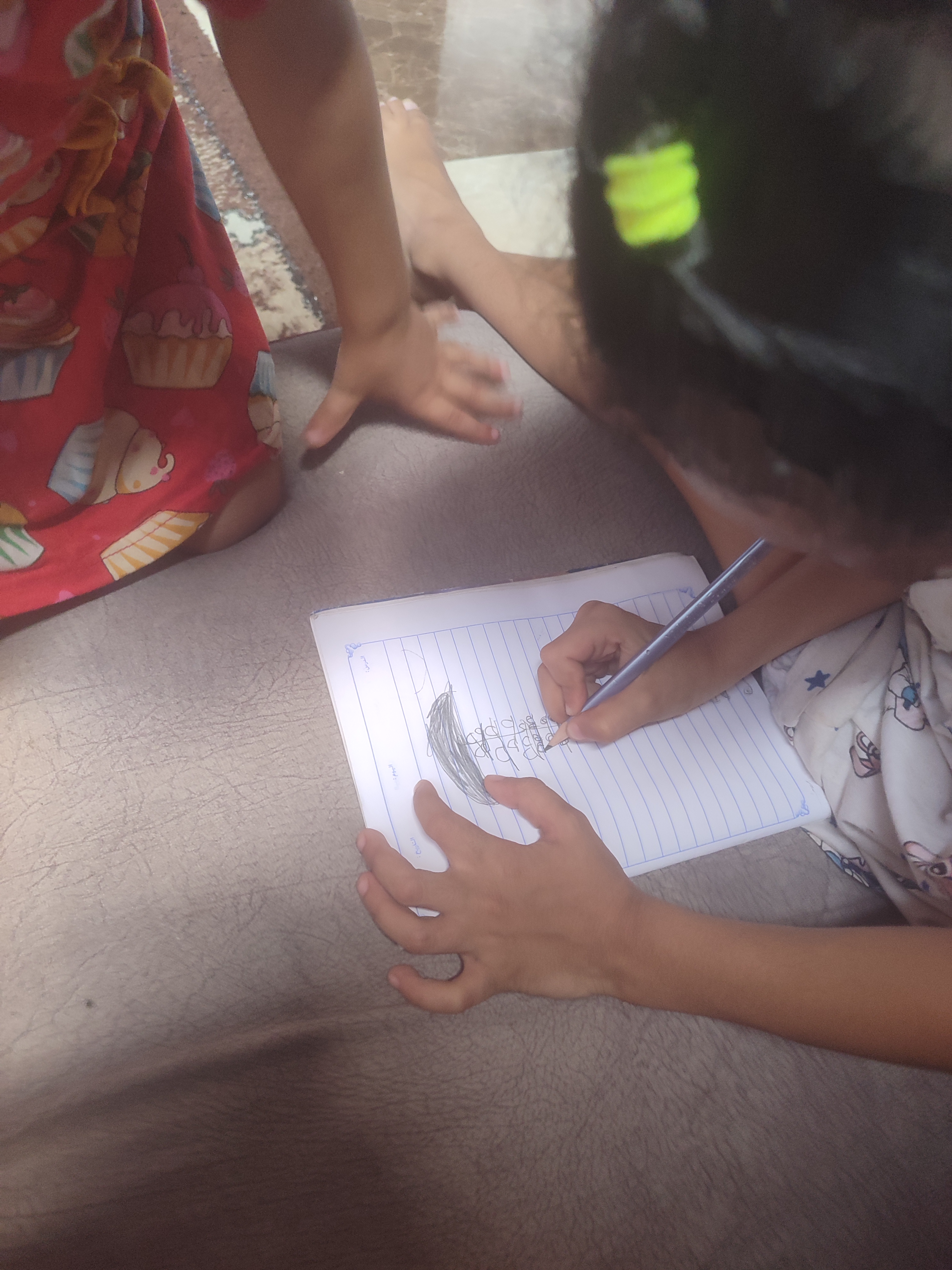 A child, drawing on a piece of paper, as another child watches